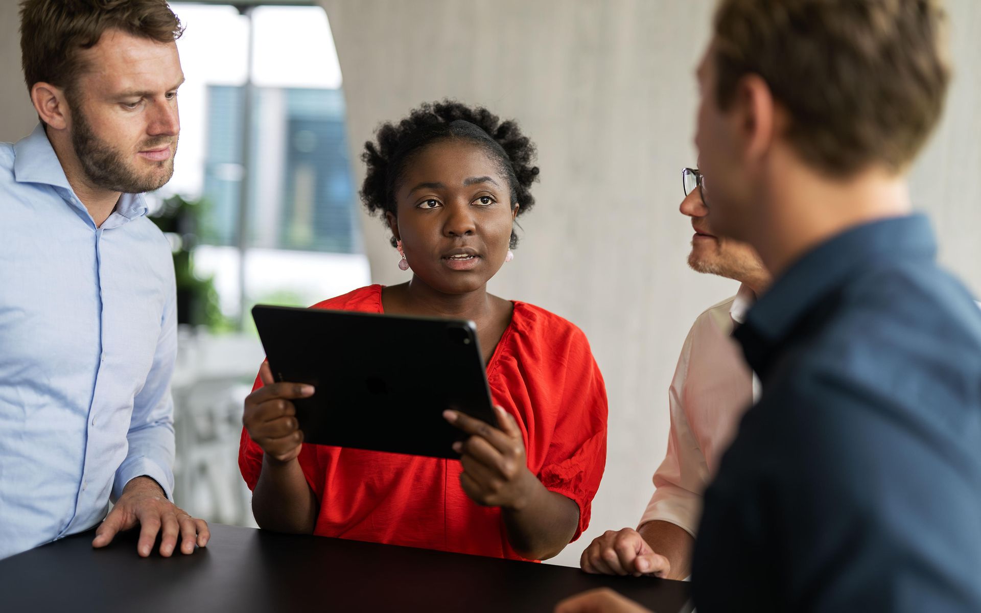 Frau mit Tablet-PC im Gespräch mit drei Männern