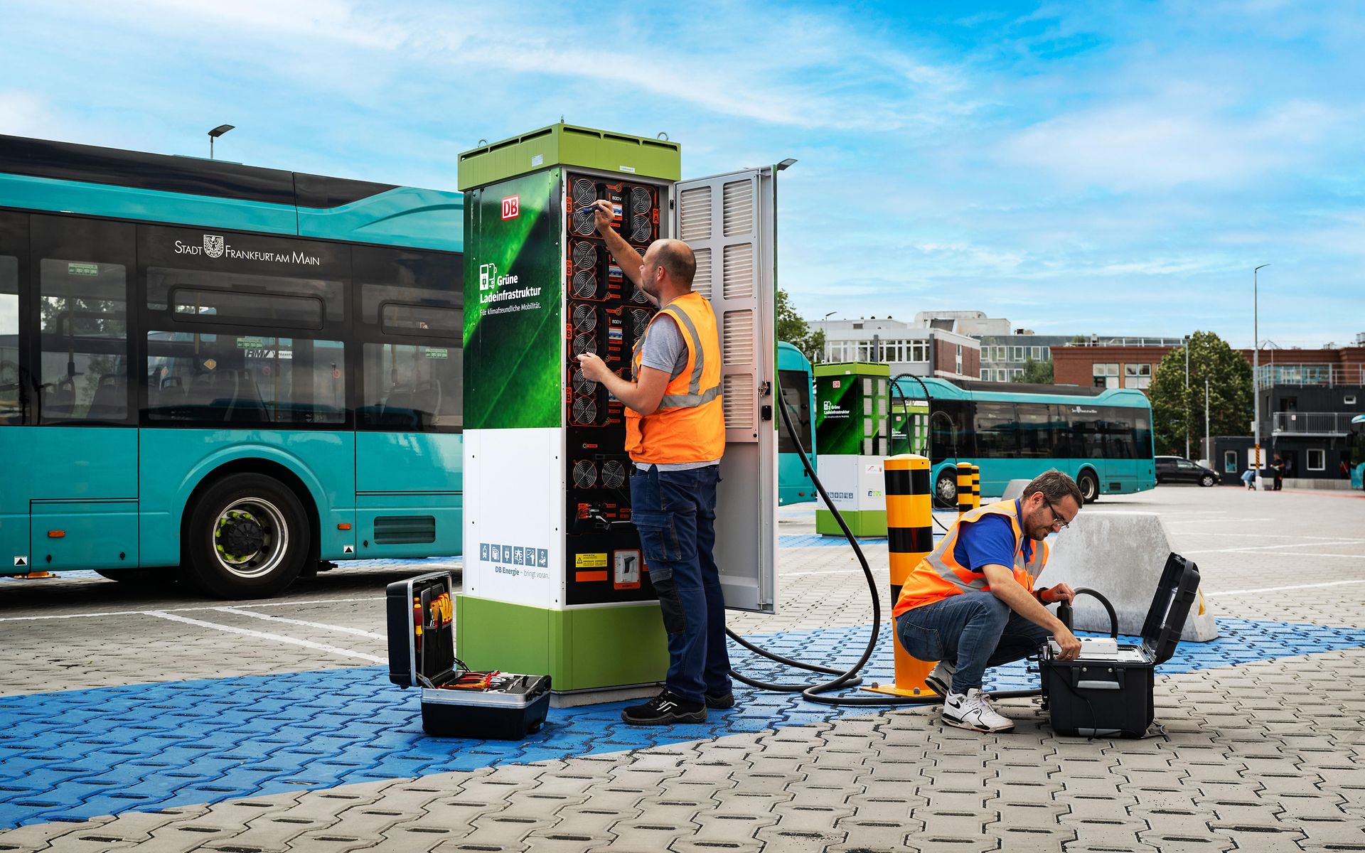 Techniker vor geöffneter Ladesäule und Busse im Hintergrund