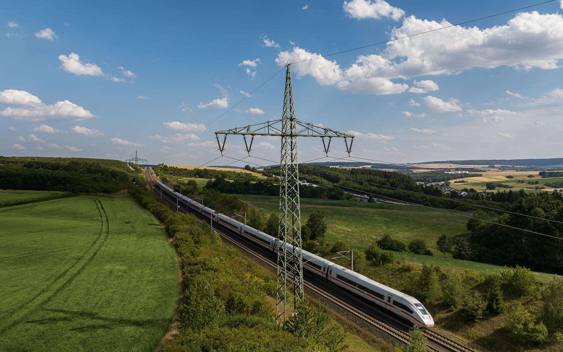 Bahnstrommast in grüner Landschaft mit ICE 4
