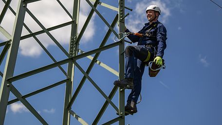 Mann mit Helm klettert auf Bahnstrommast