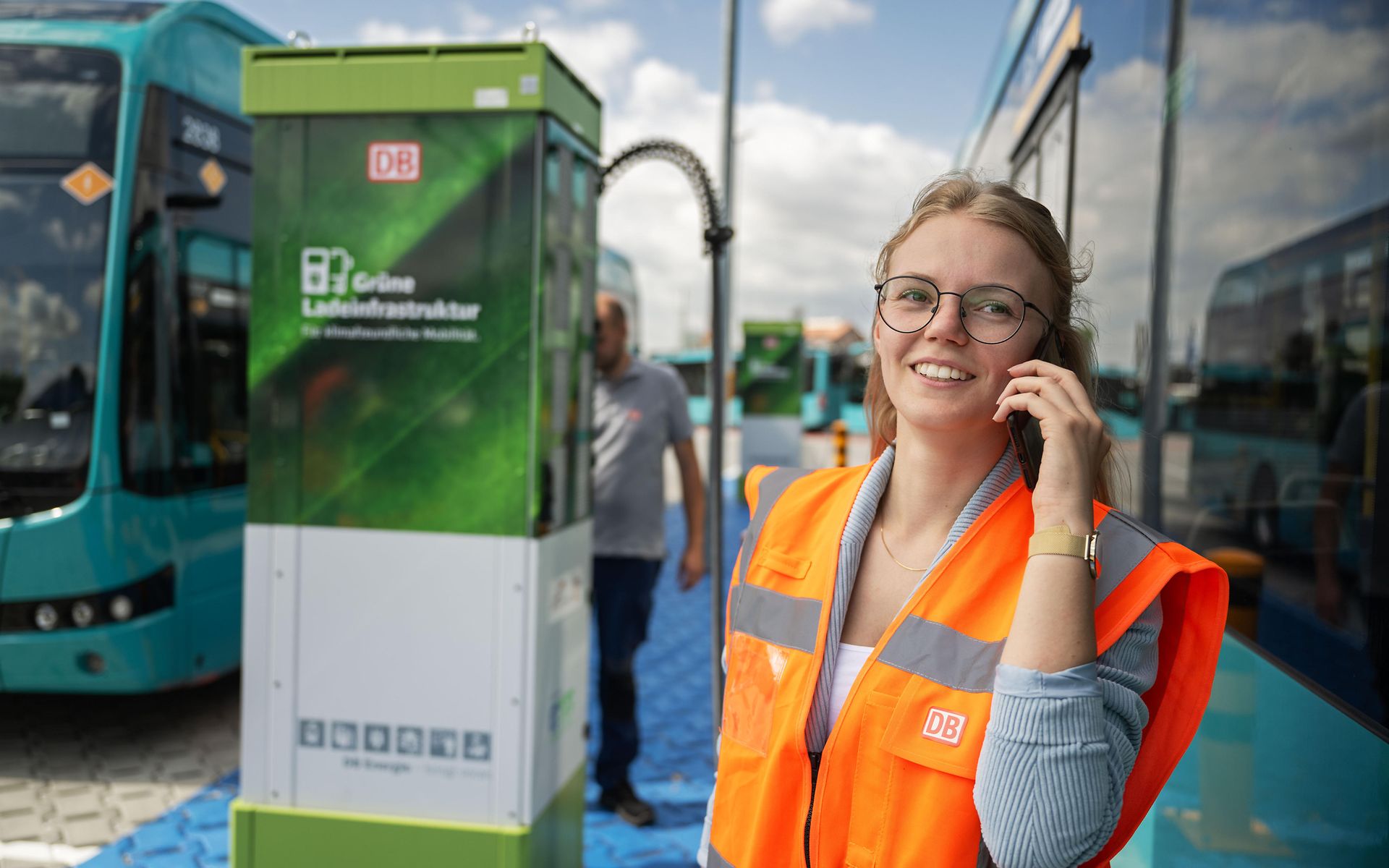 Frau mit Warnweste telefoniert vor einer Ladesäule