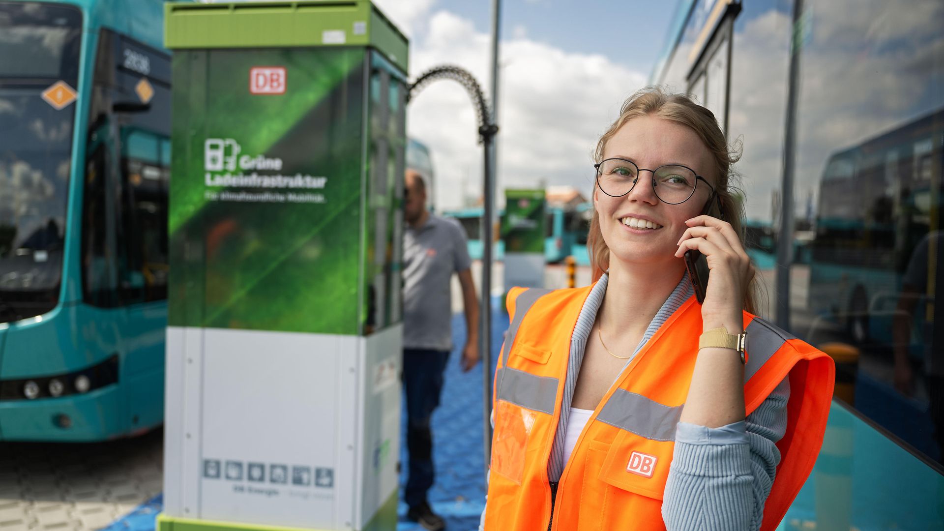 Frau mit Warnweste telefoniert vor einer Ladesäule