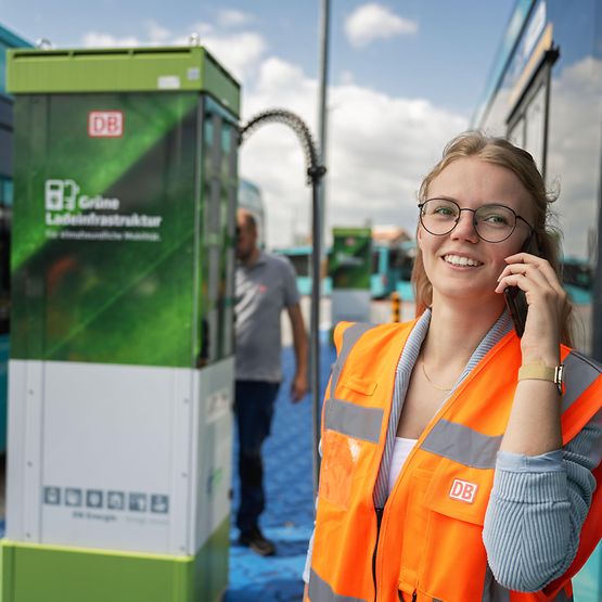 Frau mit Warnweste telefoniert vor einer Ladesäule