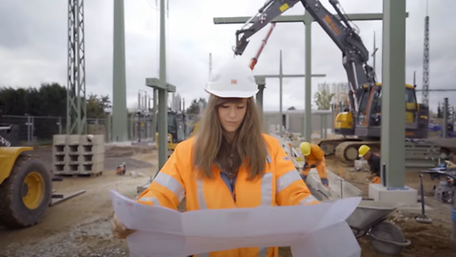Frau mit Helm und Bauplan auf Baustelle