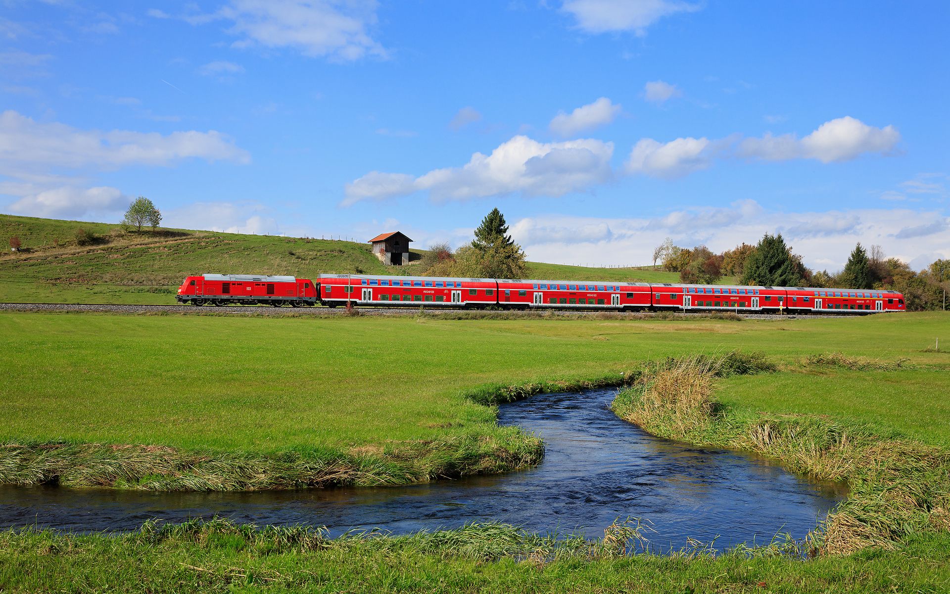 Doppelstöckiger Dieselzug in grüner Landschaft mit Bachlauf im Vordergrund
