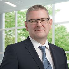 Mann mit Anzug, Hemd und Krawatte schaut in die Kamera