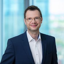 Mann mit Anzug, Hemd und Brille lächelt in die Kamera