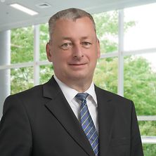 Mann mit Anzug, Hemd und Krawatte schaut in die Kamera